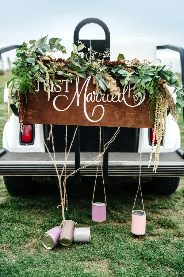 A Wedding Signboard just married, on a golf carriage adorned with flowers and tin cans on the golf course. Wedding ceremony and transportation.