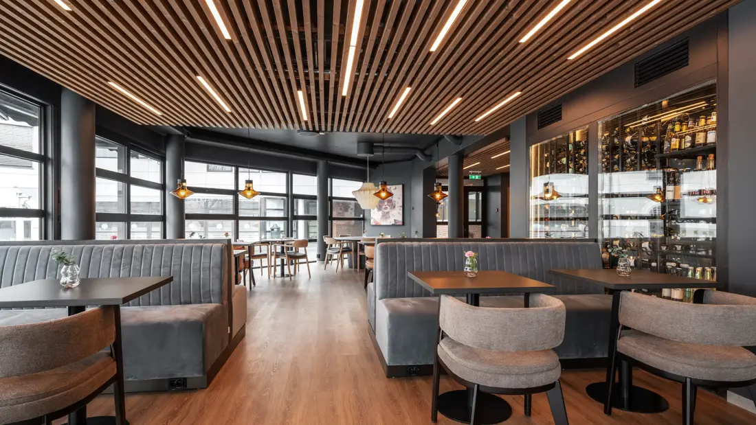 Frokostsal med store vinduer på den ene siden med dagslys strømmende inn. Hengende taklamper og brunt tregulv.