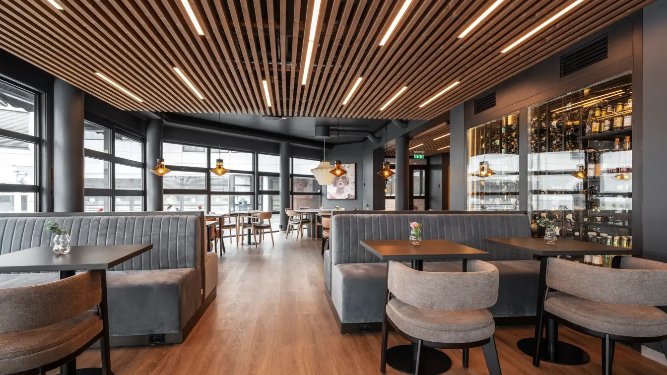 Frokostsal med store vinduer på den ene siden med dagslys strømmende inn. Hengende taklamper og brunt tregulv.