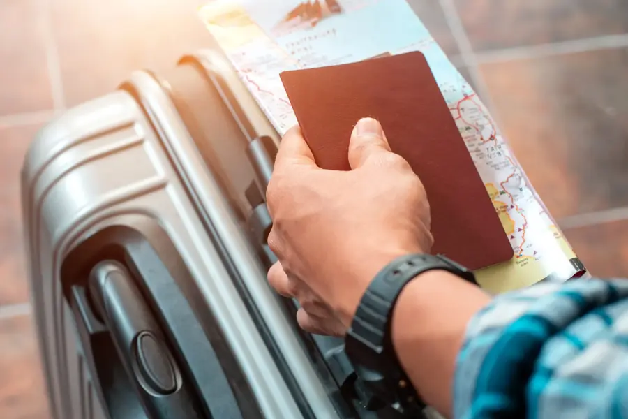 Hånd som holder pass og kart oppå en koffert