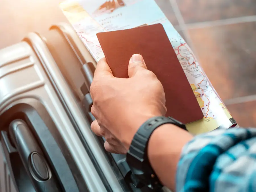 Hånd som holder pass og kart oppå en koffert