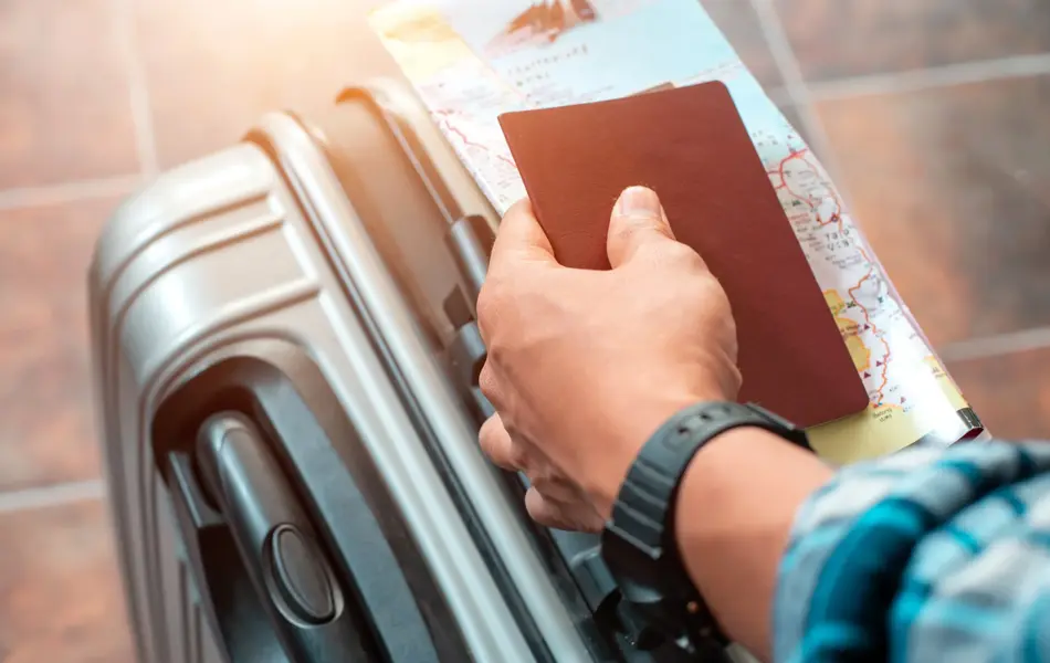 Hånd som holder pass og kart oppå en koffert