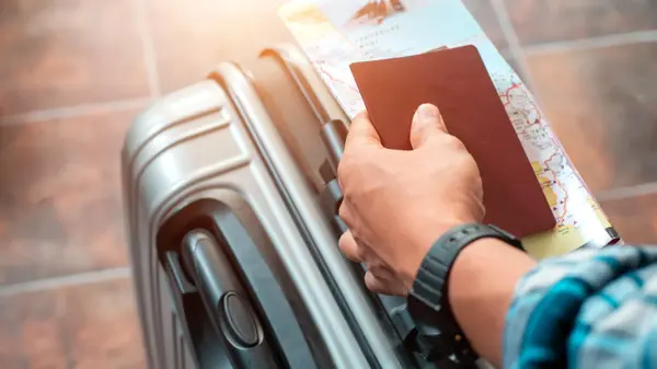 Hånd som holder pass og kart oppå en koffert