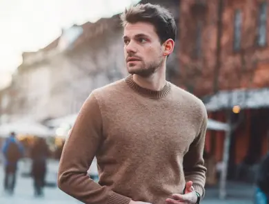 Mann i brun ullgenser poserer foran kamera utendørs på vinterlig gate 