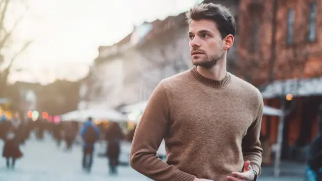 Mann i brun ullgenser poserer foran kamera utendørs på vinterlig gate 
