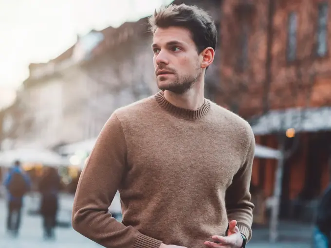 Mann i brun ullgenser poserer foran kamera utendørs på vinterlig gate 