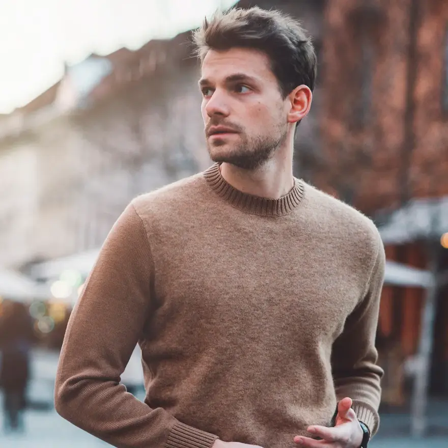 Mann i brun ullgenser poserer foran kamera utendørs på vinterlig gate 