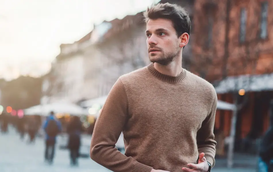 Mann i brun ullgenser poserer foran kamera utendørs på vinterlig gate 