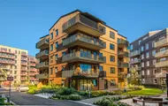 Bildet viser en blokk med leiligheter i boligprosjektet Skårerløkka PREMIUM på Lørenskog. Blokken er i lyst tre med balkonger i mørkt materiale. Det er et grønt område rundt blokken og blå himmel.