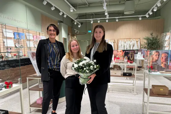 Tre damer står i butikkåpningen og holder en blomst