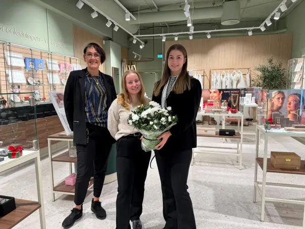 Tre damer står i butikkåpningen og holder en blomst