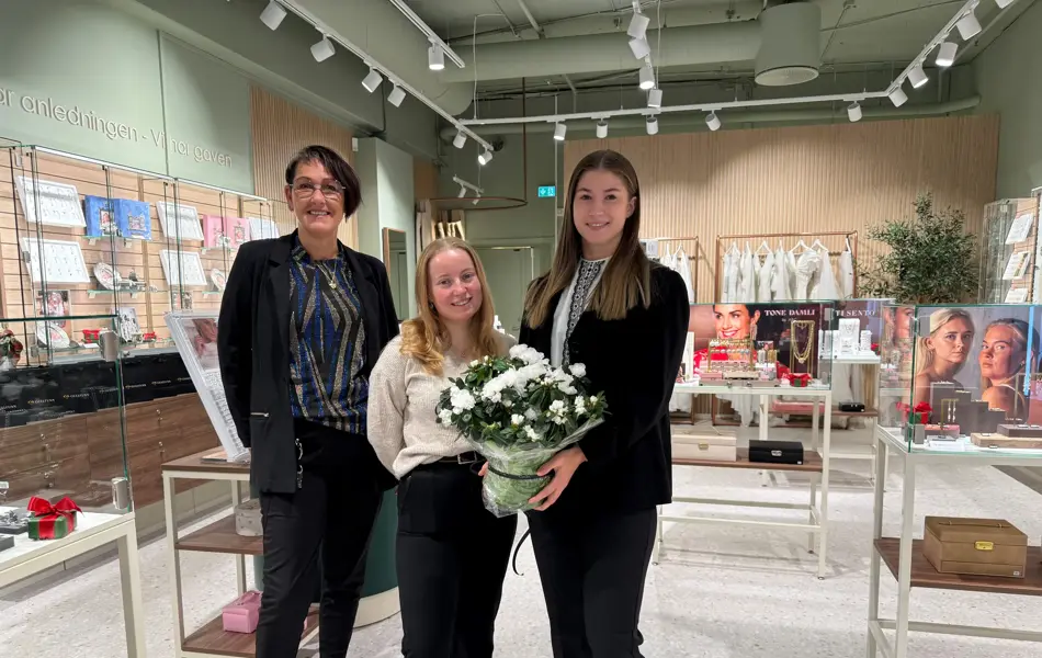 Tre damer står i butikkåpningen og holder en blomst