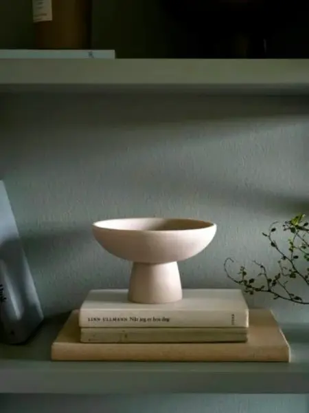 Bolle står på bøker foran en grønnmalt vegg.