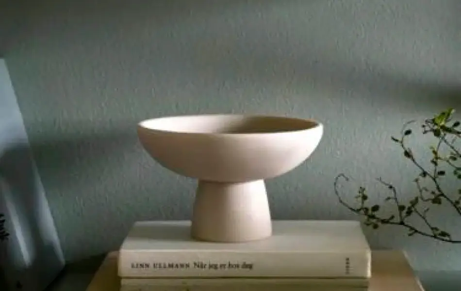 Bolle står på bøker foran en grønnmalt vegg.