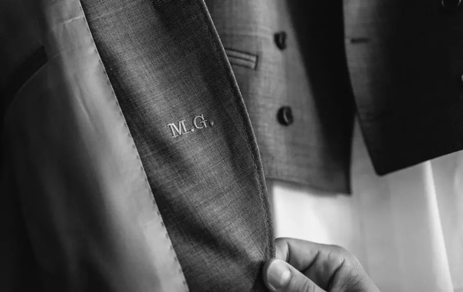 Hånd tar på en dressjakke, som er gravert med initialene M.G.