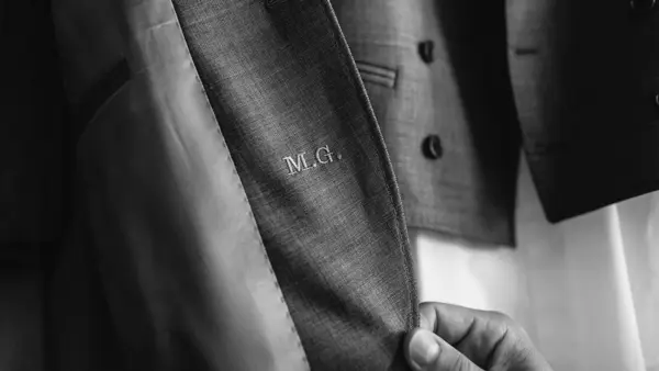 Hånd tar på en dressjakke, som er gravert med initialene M.G.