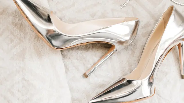 Et par høyhælte sko i sølv på et hvitt teppe.