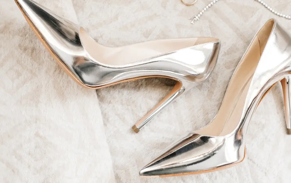 Et par høyhælte sko i sølv på et hvitt teppe.