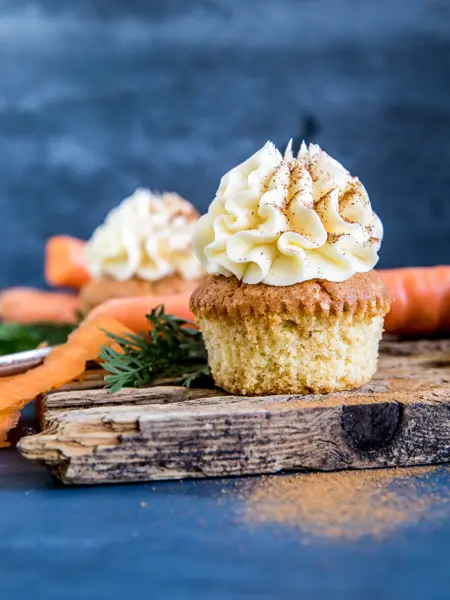 Gulerotmuffins med topping på trefjøl omringet av gulerøtter og grønt, nærbilde