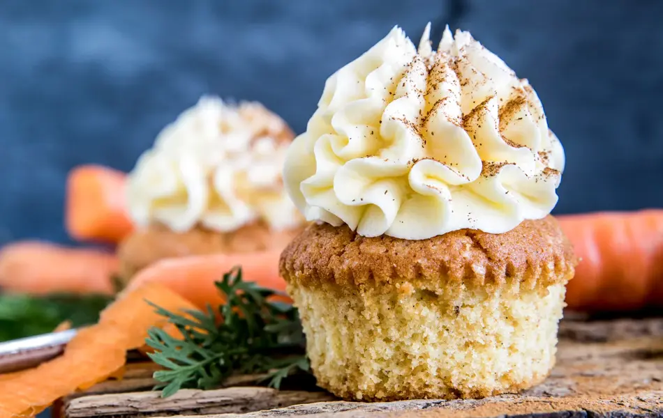 Gulerotmuffins med topping på trefjøl omringet av gulerøtter og grønt, nærbilde