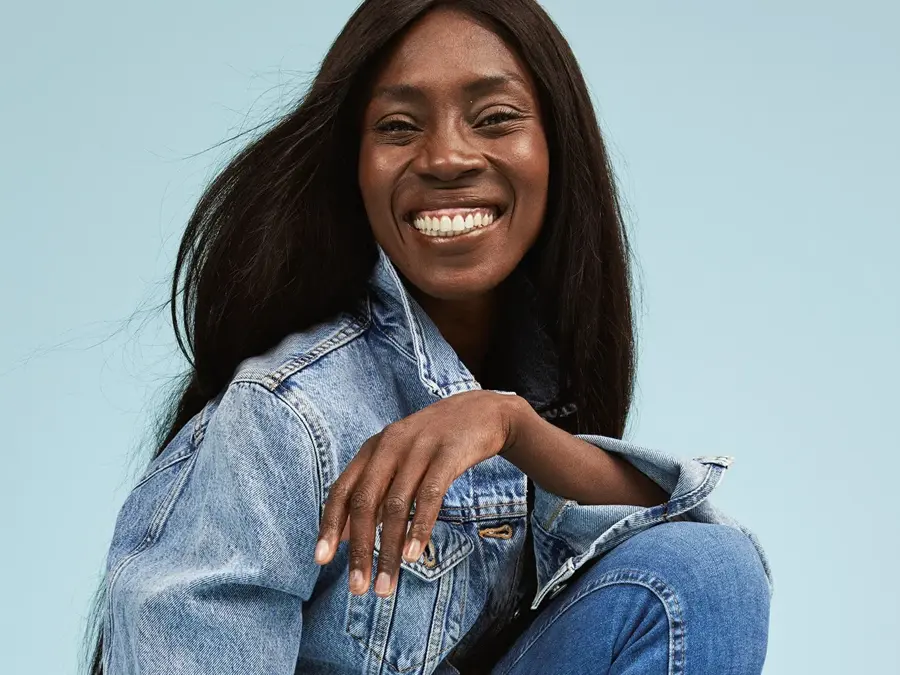 Damemodell med langt sort hår og stort smil i jeansjakke og skinny jeans fra Cubus