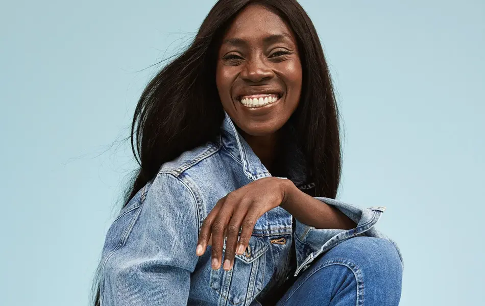 Damemodell med langt sort hår og stort smil i jeansjakke og skinny jeans fra Cubus