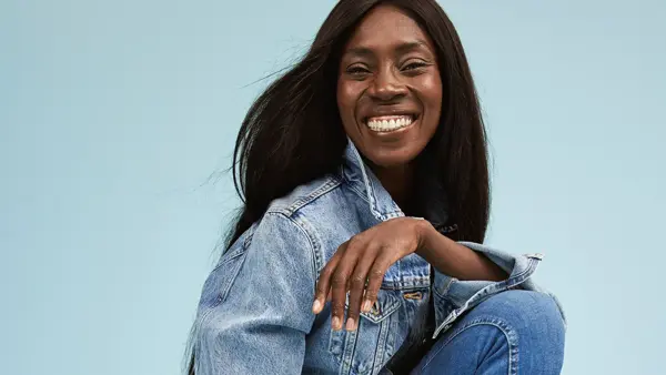 Damemodell med langt sort hår og stort smil i jeansjakke og skinny jeans fra Cubus