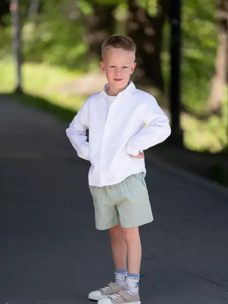 Liten gutt i hvit skjorte, grønn shorts, beige tøysko