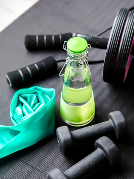 Selective focus on glass water bottle cap. Consuming fresh pure water during workout concept. Bottle on exercise mat with other training equipment. Keep hydrated.