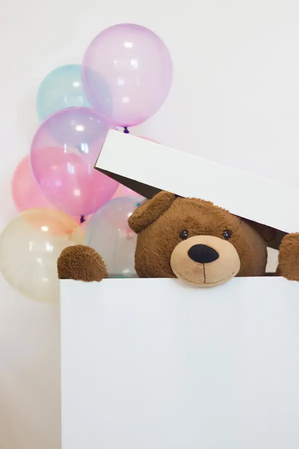 big teddy bear in a paper box with balloons on a white background. surprise for Valentine's Day. idea of celebration and gift.