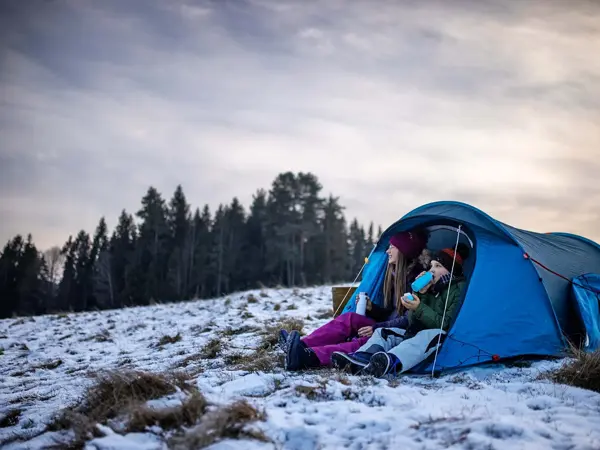 To unger som sitter i en teltåpning i delvis snølandskap