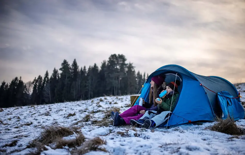 To unger som sitter i en teltåpning i delvis snølandskap