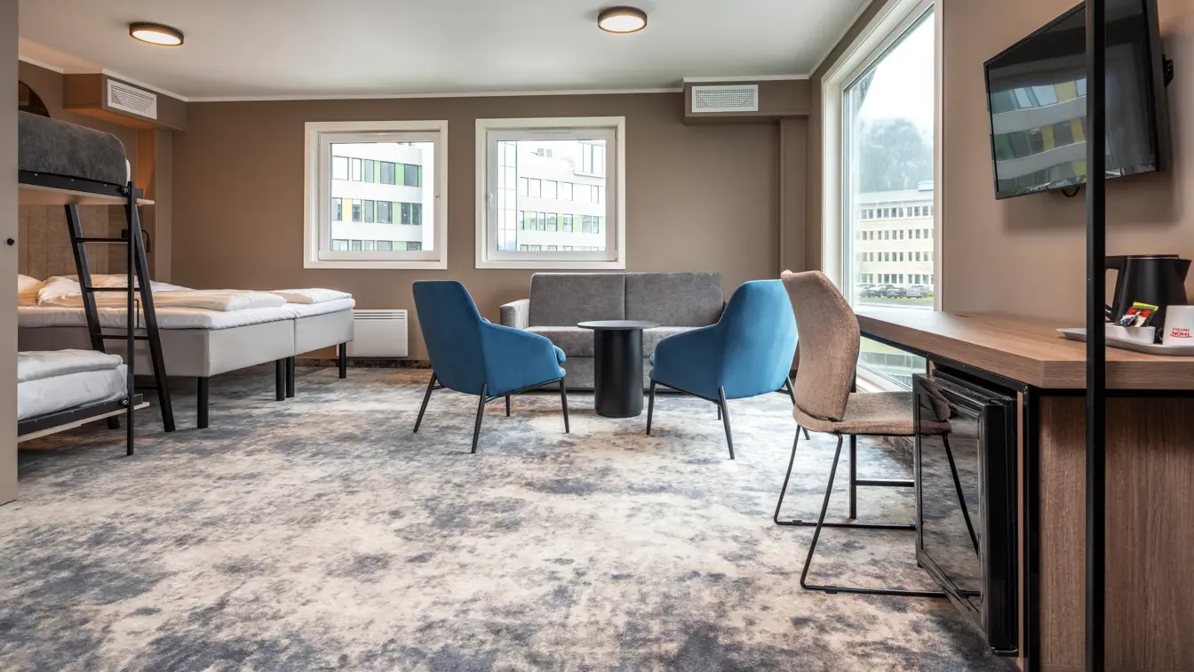 Business rom med dobbeltseng, oppredd køyeseng, sittegruppe, skrivebord med tilhørende stol og vegghengt TV.