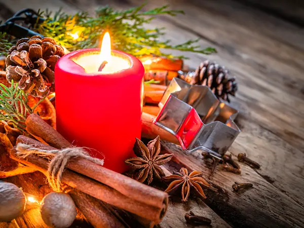 Christmas backgrounds: red burning Christmas candle shot on rustic wooden table. Cinnamon sticks, star anise, cloves and nutmeg are around the candle. The composition is at the left of an horizontal frame leaving useful copy space for text and/or logo at the right. Predominant colors are red and brown. High resolution 42Mp studio digital capture taken with Sony A7rII and Sony FE 90mm f2.8 macro G OSS lens