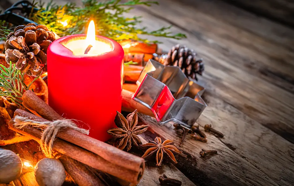 Christmas backgrounds: red burning Christmas candle shot on rustic wooden table. Cinnamon sticks, star anise, cloves and nutmeg are around the candle. The composition is at the left of an horizontal frame leaving useful copy space for text and/or logo at the right. Predominant colors are red and brown. High resolution 42Mp studio digital capture taken with Sony A7rII and Sony FE 90mm f2.8 macro G OSS lens