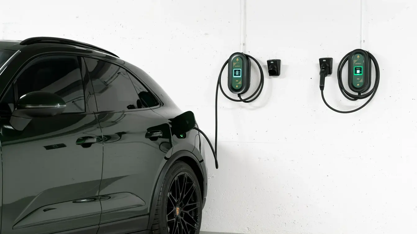 Bakdelen av en mørk bil står parkert i en garasje med to ladekabler på en hvit vegg.