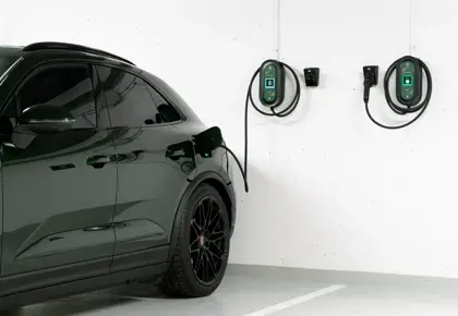 Bakdelen av en mørk bil står parkert i en garasje med to ladekabler på en hvit vegg.