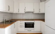 Kjøkken med hvite skap, trebenkeplate, flislagt vegg, komfyr, stekeovn og oppvaskmaskin fra Bosch.