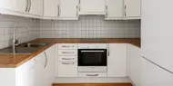 Kjøkken med hvite skap, trebenkeplate, flislagt vegg, komfyr, stekeovn og oppvaskmaskin fra Bosch.