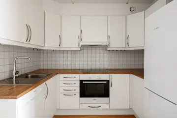 Kjøkken med hvite skap, trebenkeplate, flislagt vegg, komfyr, stekeovn og oppvaskmaskin fra Bosch.