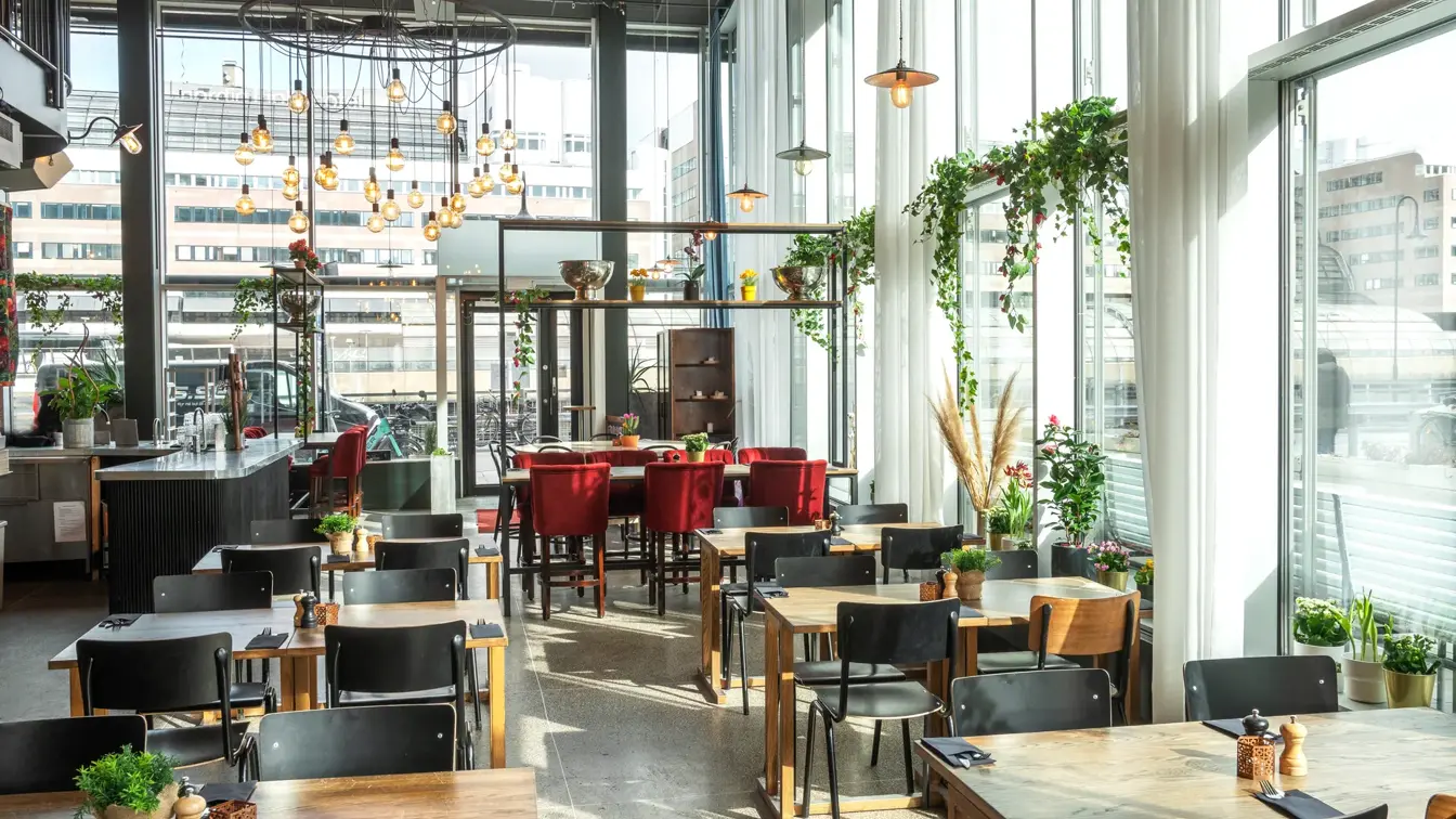 Retaurant med gulv-til-tak-vinduer på to sider, spisebord med fire eller seks tilhørende stoler, barddisk.