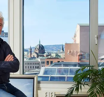 Mann sitter foran et vindu i et kontormiljø med bybildet i bakgrunnen