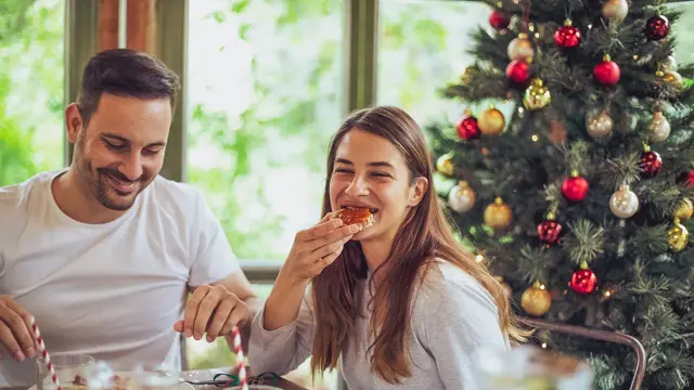 dame og mann som spiser julefrokost med juletre i bakgrunnen