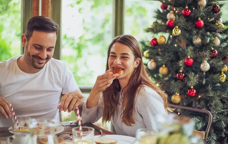 dame og mann som spiser julefrokost med juletre i bakgrunnen