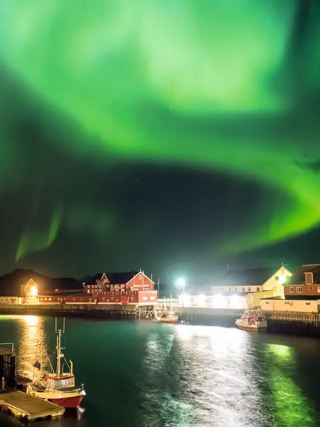 Nordlys på himmelen med bebyggelse, vann og båt i Lofoten