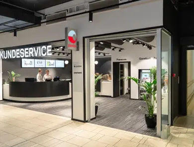 Bilde av Kundeservice lokale med skilt Posten og 2 ansatte bak disken som har 4 digitale skjermer på bakveggen