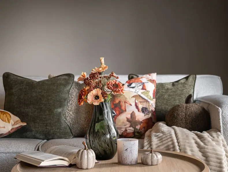 Stuebord med vase, blomster, pyntegresskar og dekorative puter i høstfarger.