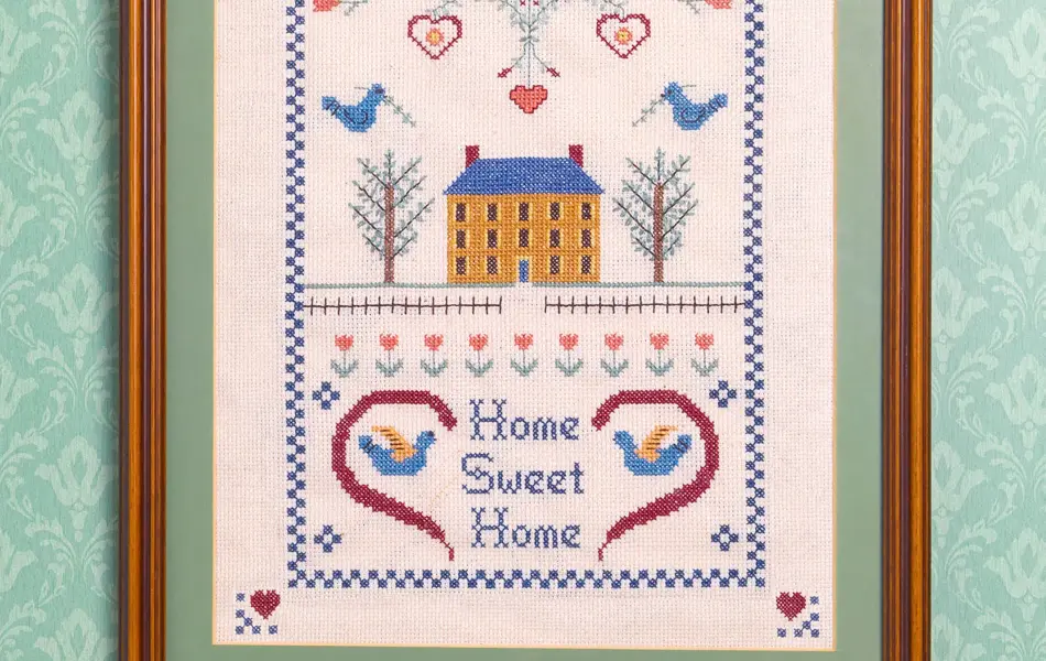 Broderitavle med “home sweet home” på en tapetsert vegg