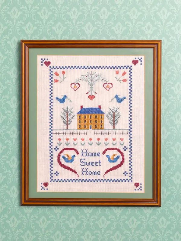 Broderitavle med “home sweet home” på en tapetsert vegg