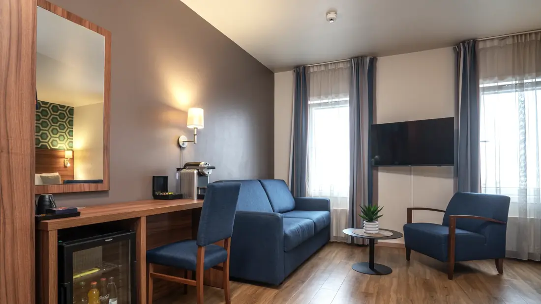 Superiorrom på Thon Partner Hotel Horten med skrivebrod, minibar, speil på vegg, blå sofa, blåe stoler, nespressomaskin, TV, avlastningsbord, to vinduer, parkettgulv.